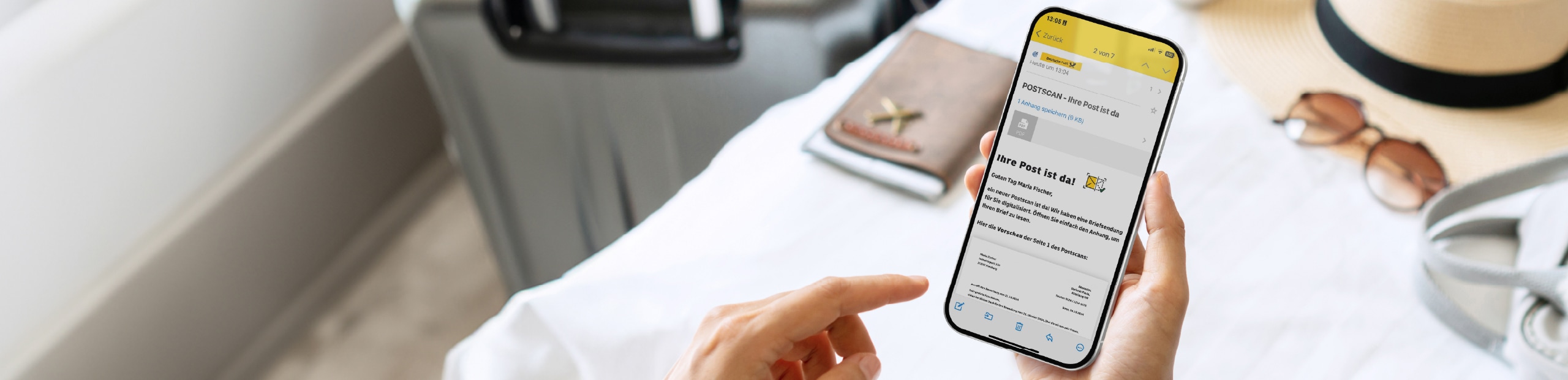 Handy mit Postscan Nachricht im Vordergrund, Reiseutensilien im Hintergrund